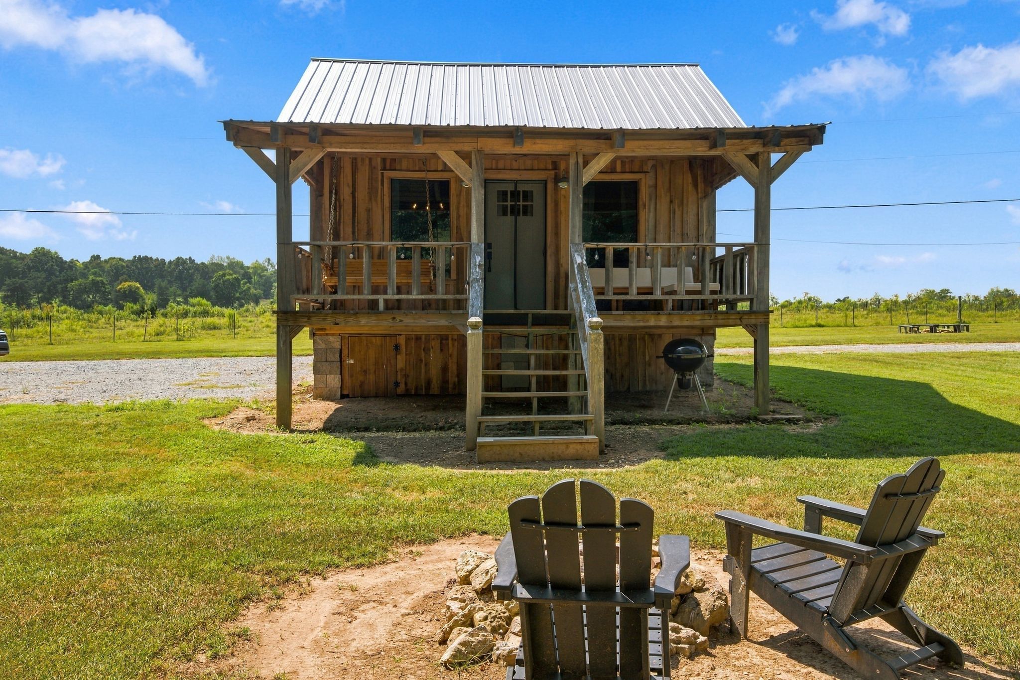 A wooden cabin with a porch, a grill, and two Adirondack chairs.