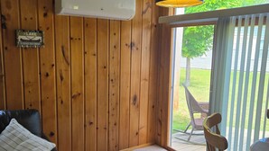 A room with wooden walls, a ceiling fan, a window with a view of greenery, a black leather couch, and a dining table with chairs. - Rocky Racoon's Rustic Retreat at Sage Lake!  Dock slip & tons of fun await!! (Hale)