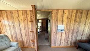 A room with wooden paneling, a grey sofa, and a dining area in the background. - Rocky Racoon's Rustic Retreat at Sage Lake!  Dock slip & tons of fun await!! (Hale)