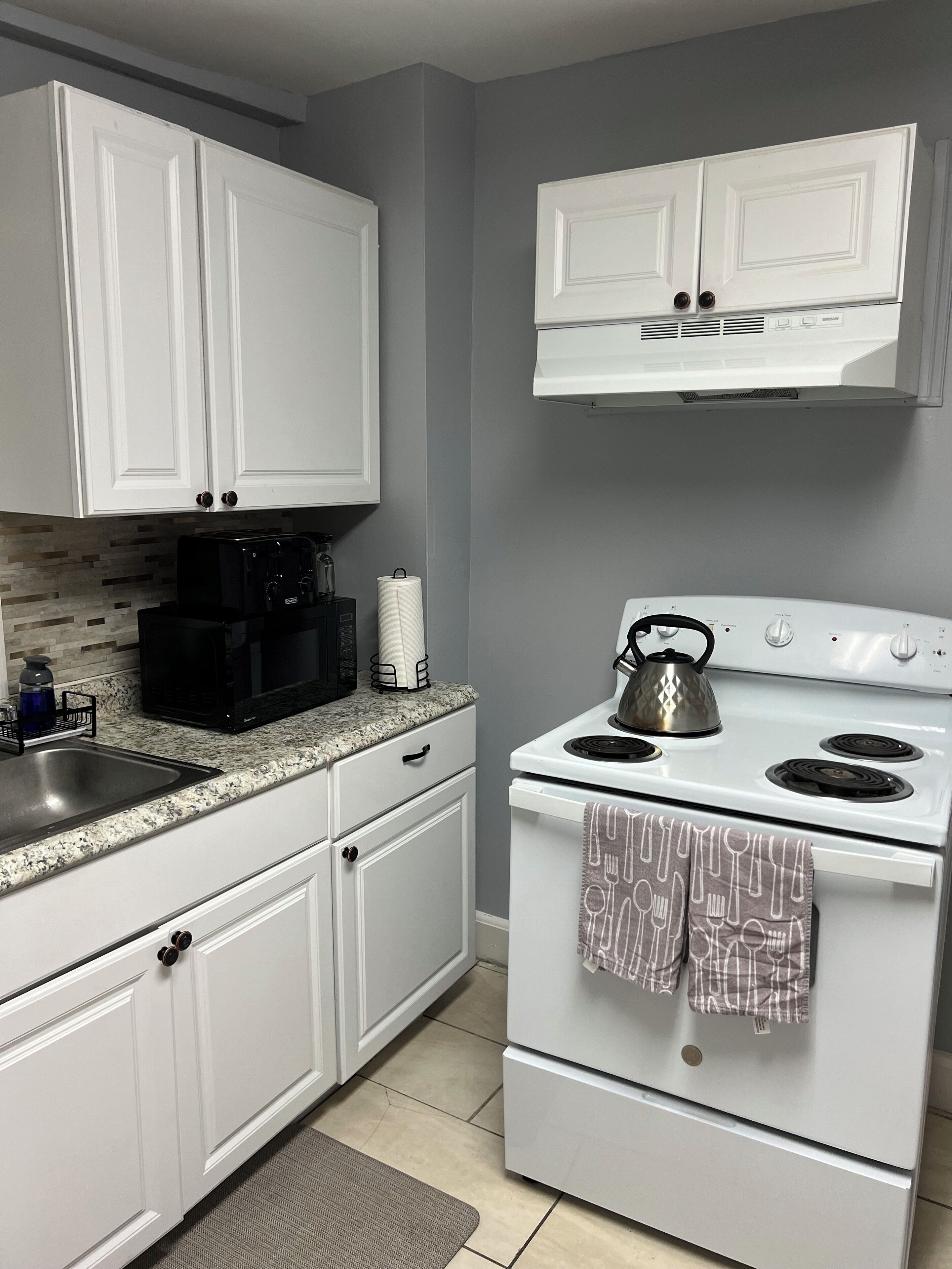 A kitchen with white cabinets, a stove, a kettle, and a coffee maker.