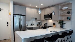 A modern kitchen with stainless steel appliances, a white countertop, and black bar stools. - Birdies and Bears by Revelstoke Vacation (Revelstoke)