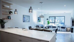 A modern kitchen with a large island, dining area with chairs, and a view of a snowy landscape through large windows. - Birdies and Bears by Revelstoke Vacation (Revelstoke)