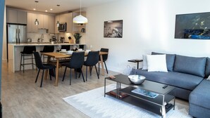 A modern living room with a grey sofa, a coffee table, and a dining area with a wooden table and chairs. - Birdies and Bears by Revelstoke Vacation (Revelstoke)