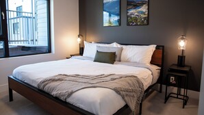 A modern bedroom with a large bed, two bedside tables, and a window with a view of a building. - Birdies and Bears by Revelstoke Vacation (Revelstoke)