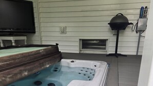 Un bain à remous avec une terrasse en bois et un téléviseur fixé au mur.