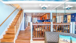 A spacious living area with a wooden staircase, a dining area with a glass partition, and a sofa with decorative pillows.