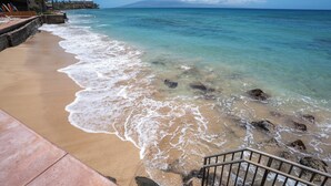 A beach with clear water, a sandy shore, and a staircase leading down to the water.
