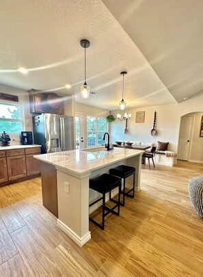 Una cocina amplia con una isla grande, electrodomésticos de acero inoxidable, iluminación colgante y suelo de madera.