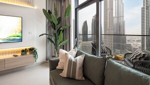 Un salon moderne avec une grande fenêtre, un téléviseur à écran plat, un canapé vert et une plante.