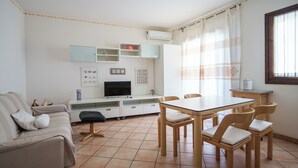Ein Wohnzimmer mit einer Couch, einem Fernseher und einem Esstisch mit Stühlen.