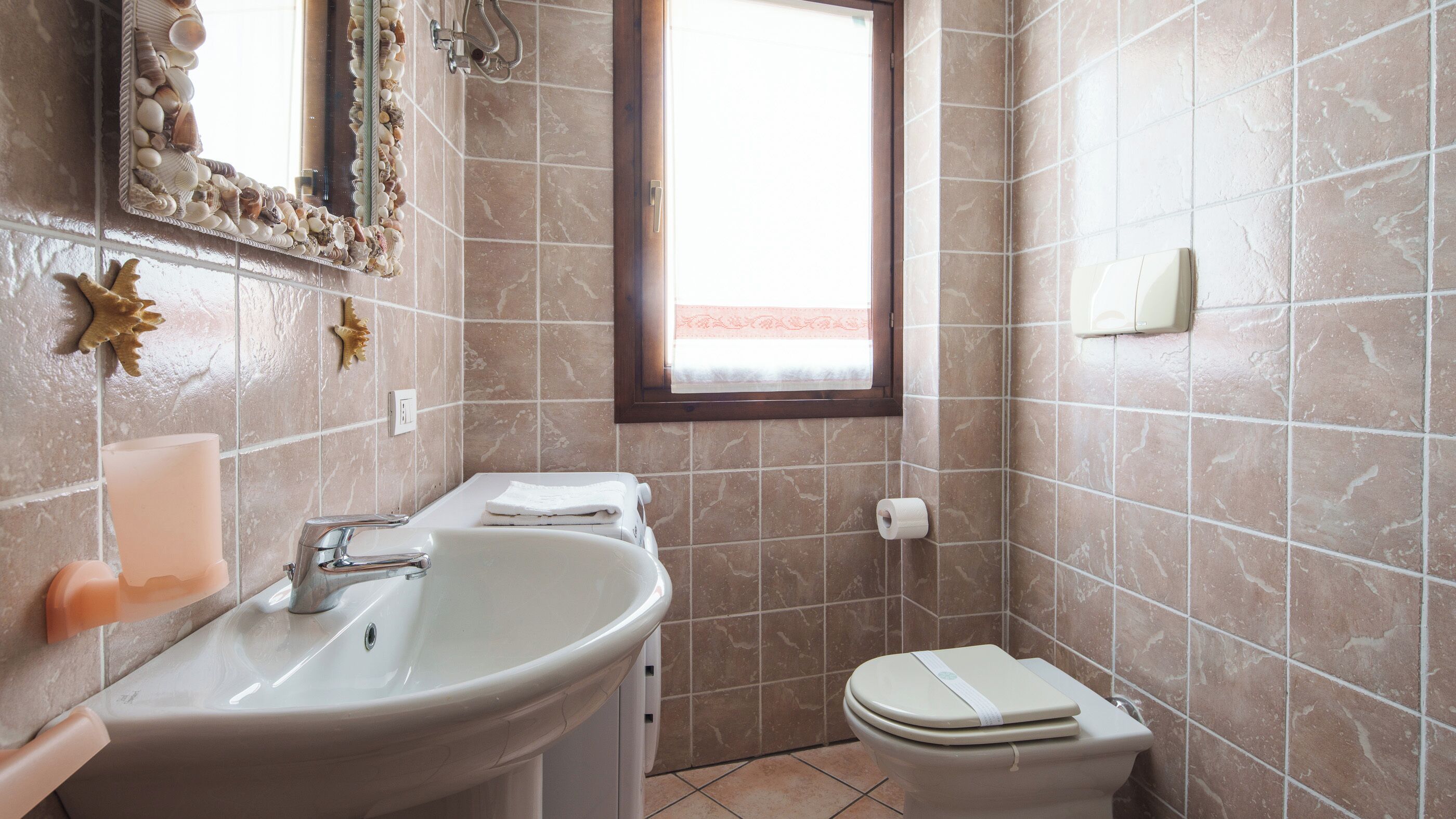 Een badkamer met een wastafel, spiegel, toilet en een raam.