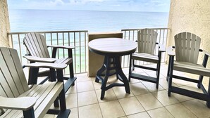 A balcony with a view of the ocean, furnished with wooden chairs and a table.