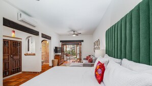 Habitación de hotel con una cama grande, un cabecero verde, un televisor y un balcón con vistas a edificios.