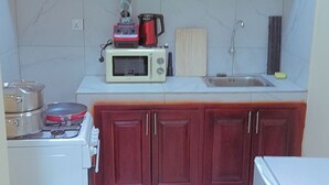 A compact kitchen with red cabinets, a microwave, a blender, and a small refrigerator. - Bosslife Apartement (Douala)