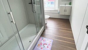 A modern bathroom with a glass shower enclosure, a toilet, a sink, and a window with a view of a building outside. - OYO Welsh Holiday Accommodation - Modern Stay (Pembroke Dock)