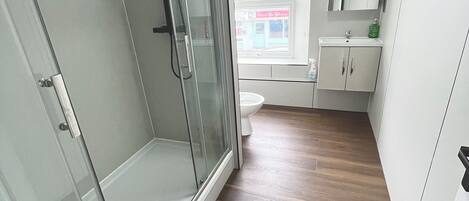 A modern bathroom with a glass shower enclosure, a toilet, a sink, and a window with a view of a building outside.