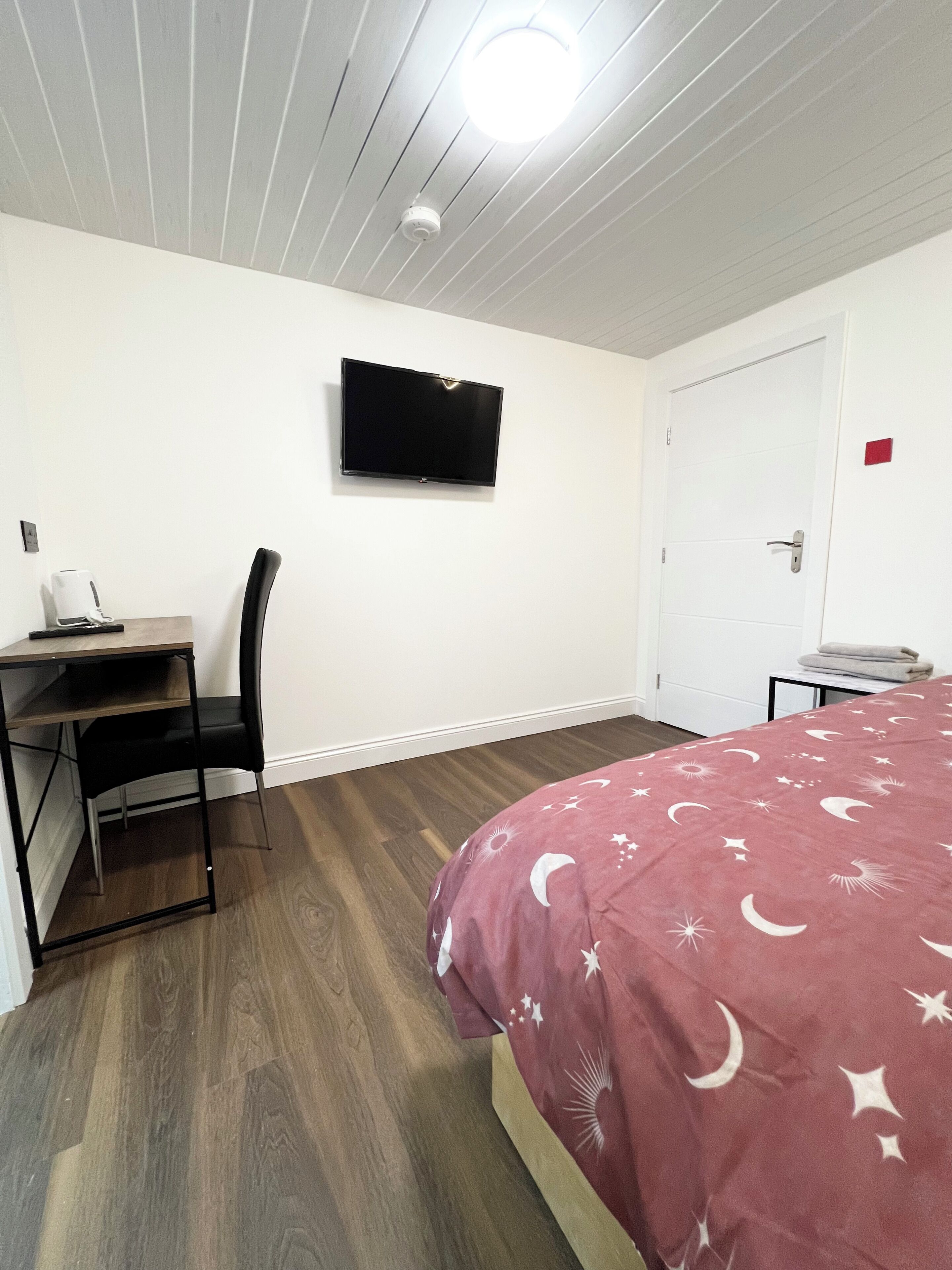 A bedroom with a bed, a desk, a chair, a television, and a door.