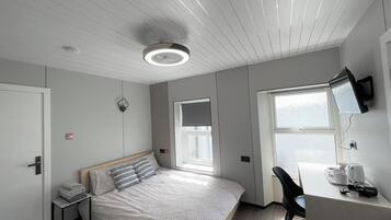 A modern hotel room with a bed, a desk, a chair, a TV, and a window.