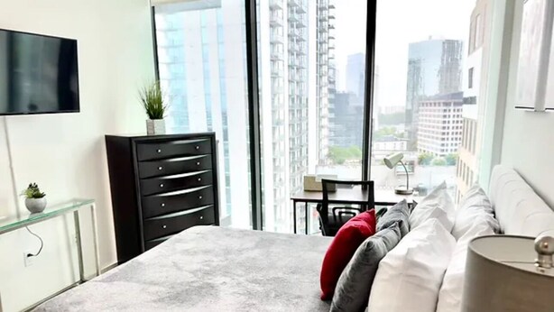 Ein modernes Schlafzimmer mit einem großen Bett, einem Schreibtisch und Blick auf hohe Gebäude.