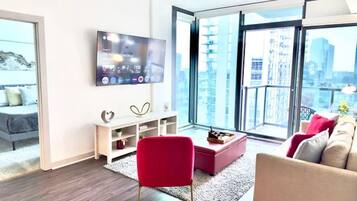 A modern living room with a large TV, a red chair, a pink ottoman, and a beige sofa.