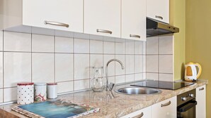 A kitchen with white cabinets, a stainless steel sink, a glass pitcher, and a kettle on the counter. - Seafront Apt on Sunny Rab Island - Neda Maslina (Kampor)