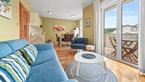 A living room with a blue sofa, a small round table, and a dining area with chairs and a table. - Seafront Apt on Sunny Rab Island - Neda Maslina (Kampor)