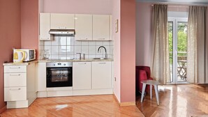 Une cuisine compacte avec des meubles blancs, un four encastré et un petit coin repas comprenant une chaise rouge et une table.