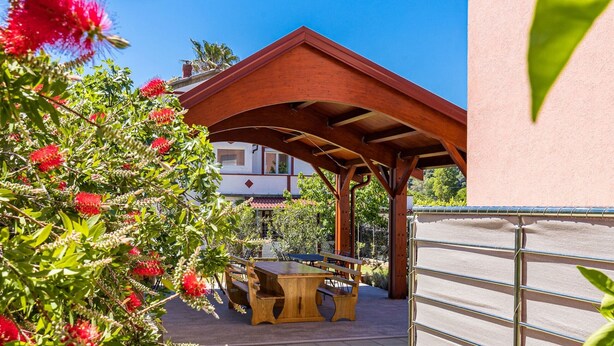 Un espace patio agrémenté d’une pergola en bois, de sièges d’extérieur et offrant une vue sur un bâtiment.