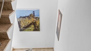 Un escalier avec une rampe métallique, un tableau représentant un paysage encadré accroché au mur et un sol carrelé.
