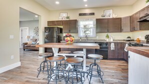 A modern kitchen with wooden cabinets, a central island with stools, a refrigerator, and a window with decorative items.