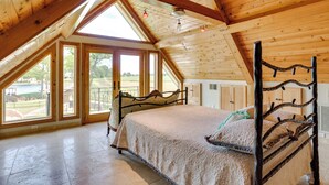 Ein Schlafzimmer mit hohen Decken, Holzboden, einem großen Bett mit Kopfteil und großen Fenstern mit Blick ins Freie.