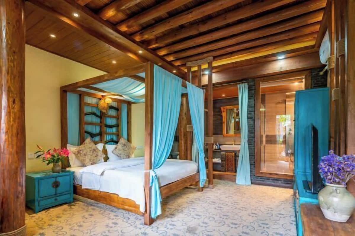 A bedroom with a four-poster bed, a nightstand, a vase with flowers, and a mirror.