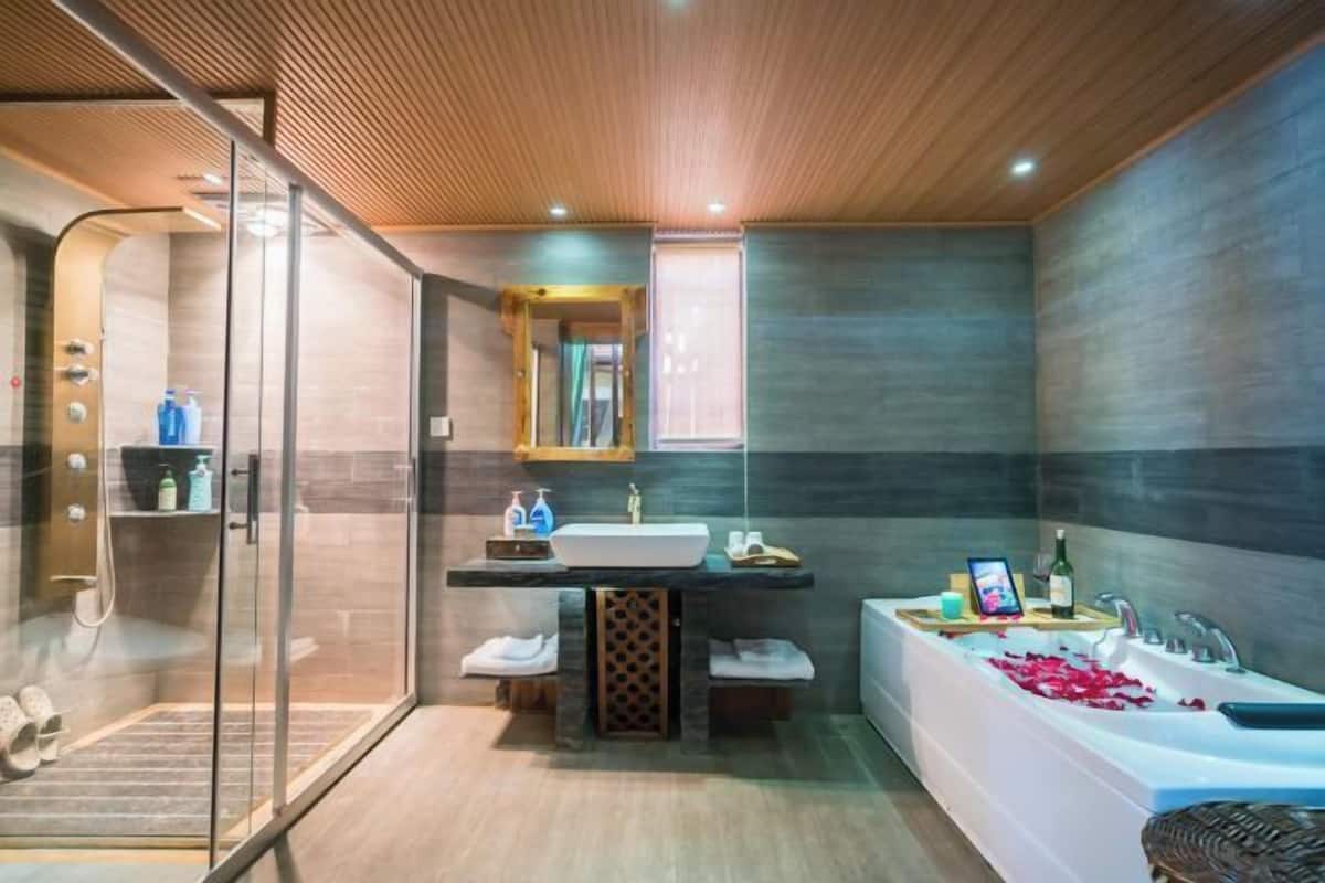 A modern bathroom with a glass shower enclosure, a large bathtub with rose petals, and a vanity with a mirror.