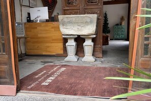 A reception area with a wooden desk, a stone bench, and a green plant. - Yun Qieman Inn· Panoramic Snow Mountain View & Golden Peak Sunrise (Old Town of Lijiang ) (Lijiang)