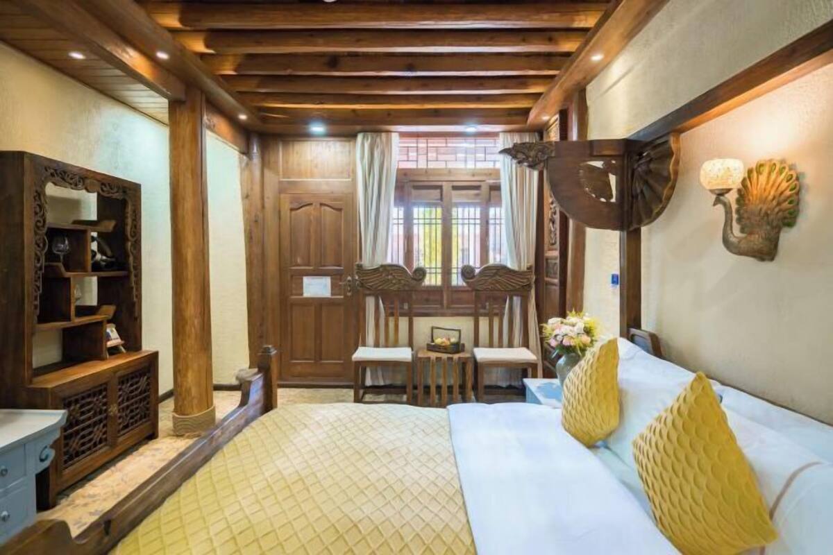 A traditional wooden room with a bed, a wooden cabinet, a table with chairs, and a window with curtains.
