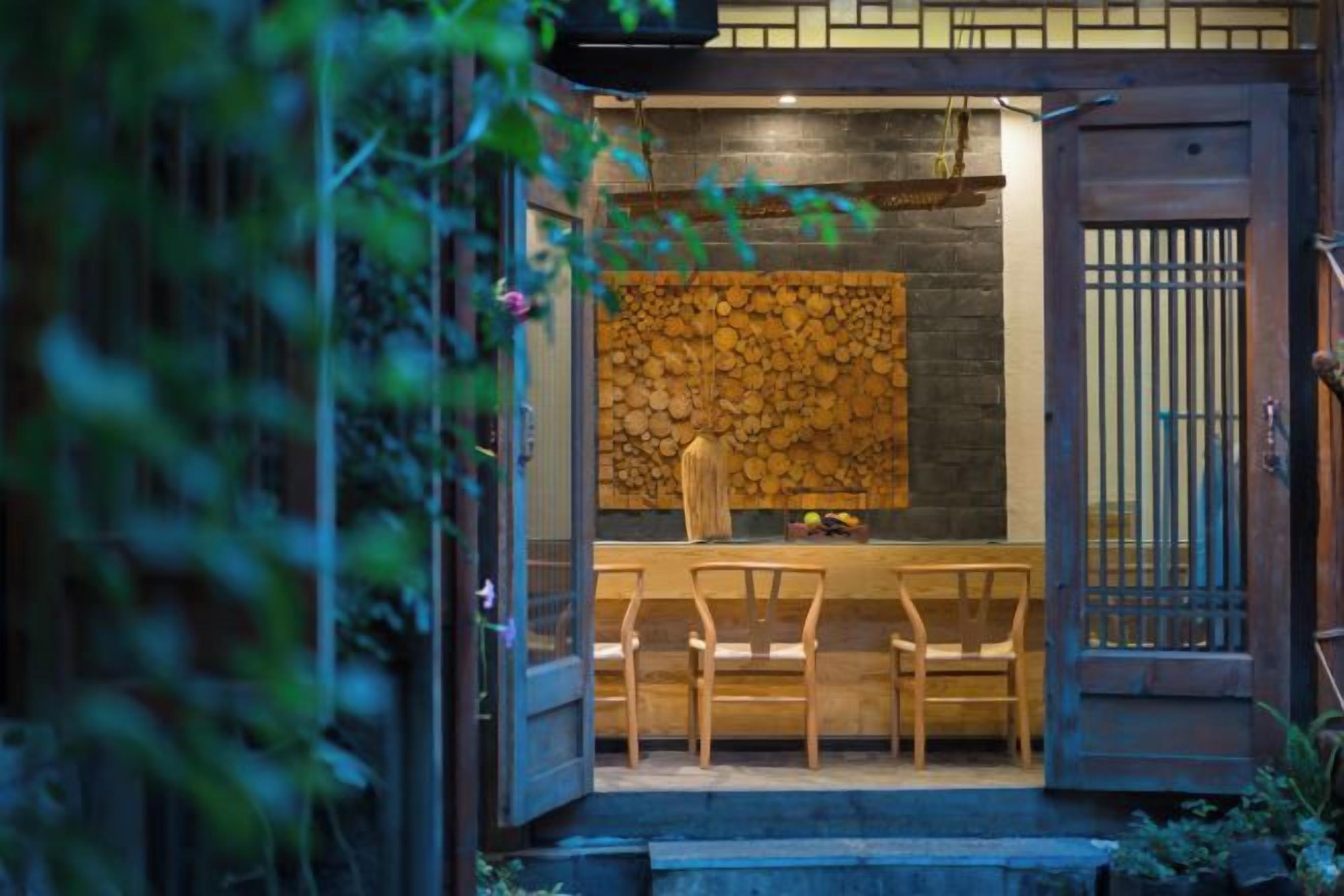 An entrance with a wooden door, a stone wall, and a seating area with chairs.