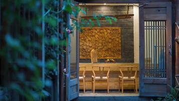 An entrance with a wooden door, a stone wall, and a seating area with chairs.