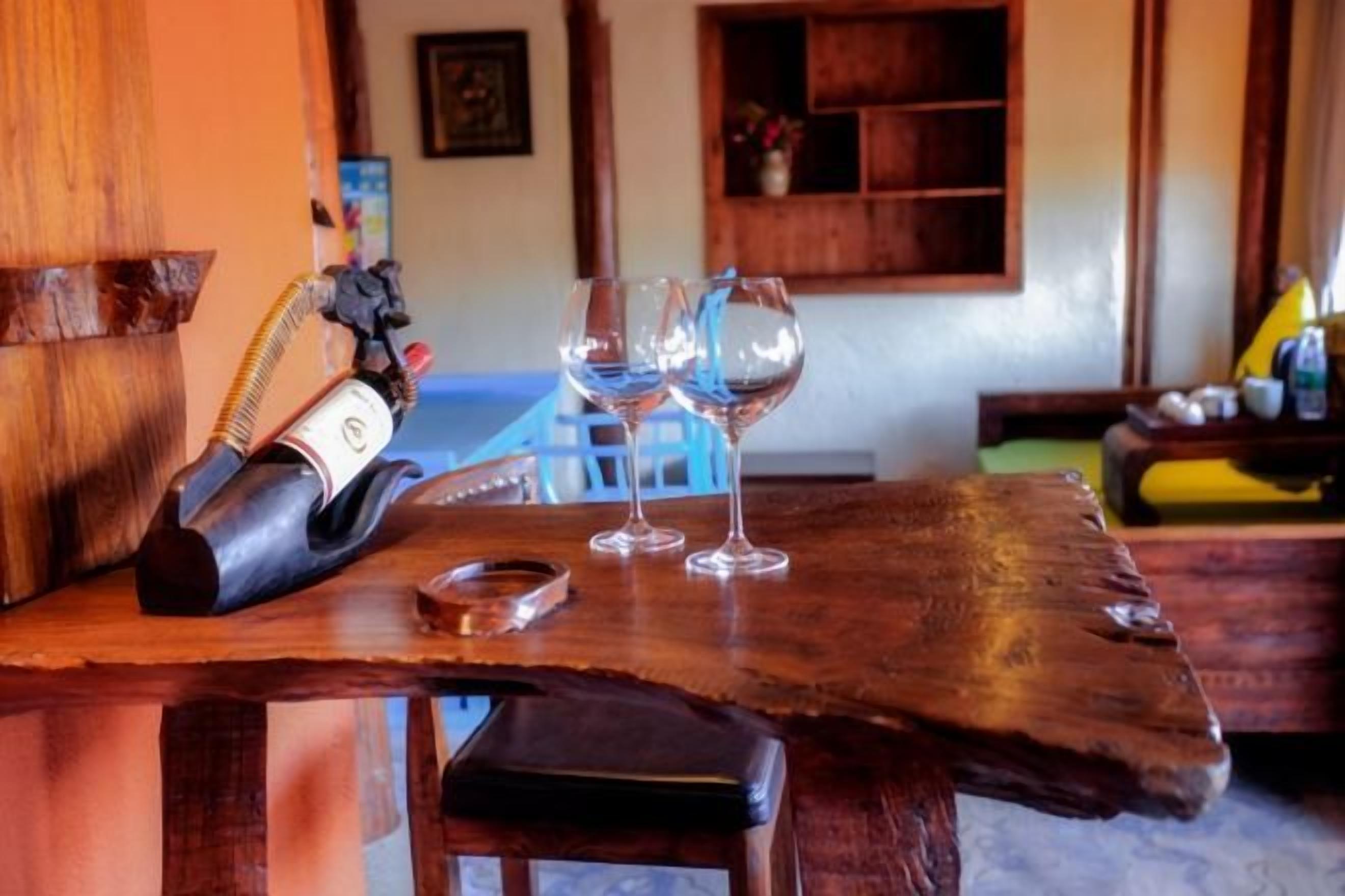 A wooden bar table with a bottle, glasses, and a small container.