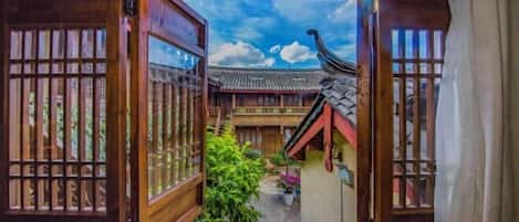 A traditional wooden gate leading to a courtyard with tiled roofs and potted plants.