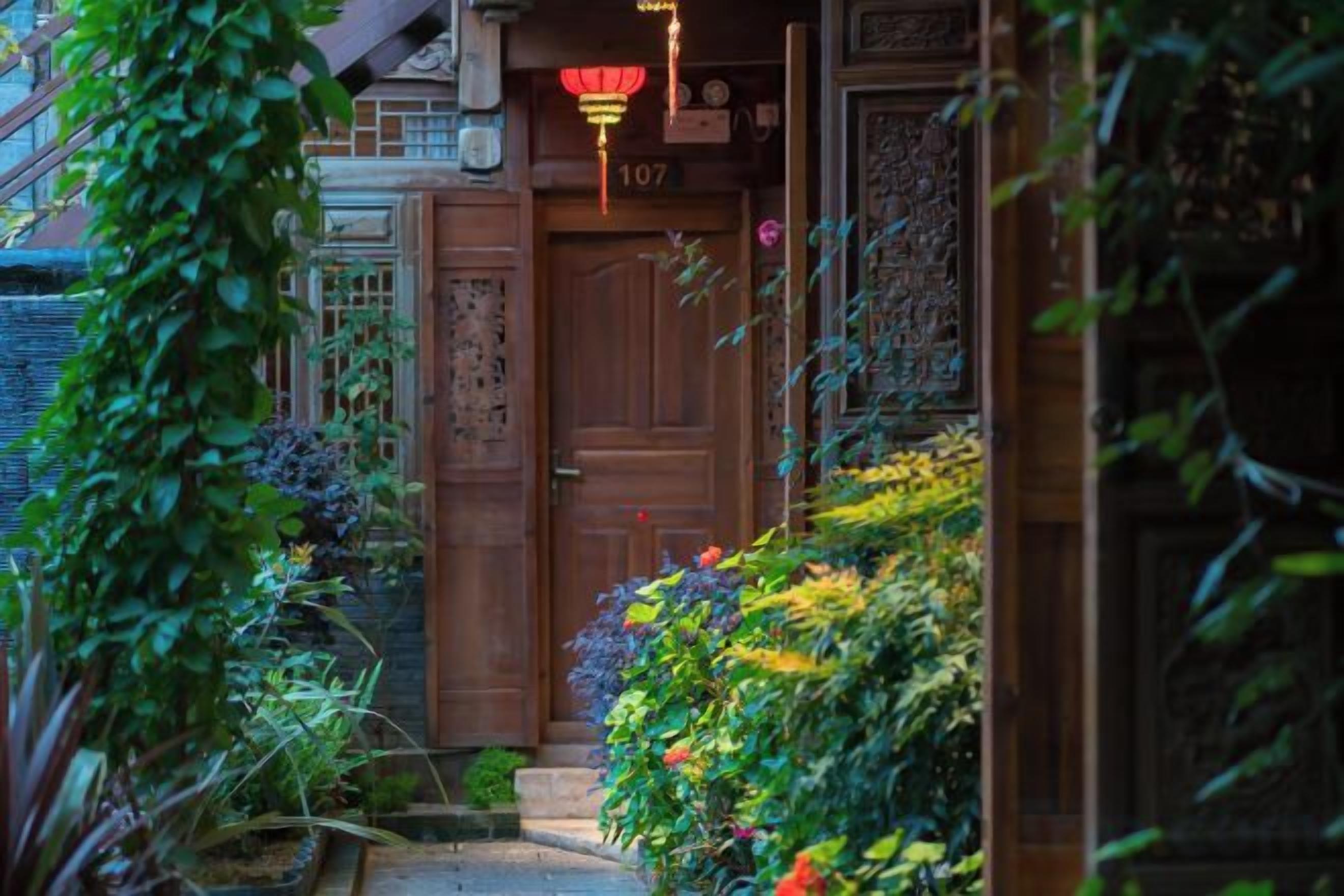 Una puerta de madera tradicional con una placa de número, rodeada de exuberante follaje y plantas decorativas.