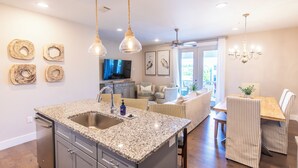 A modern kitchen with granite countertops, a built-in sink, and a dining area with striped chairs and a wooden table.