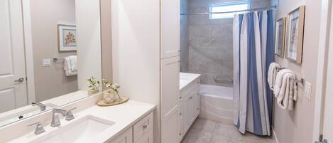 Un baño moderno con un espejo grande, dos lavamanos, una bañera y una cortina de ducha.