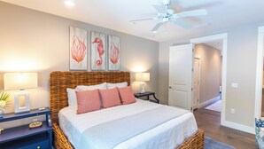 A bedroom with a large bed, two bedside tables with lamps, a ceiling fan, and artwork on the wall.