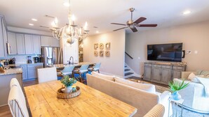 A modern kitchen with stainless steel appliances, a dining area with a wooden table, and a living room with a TV and seating.