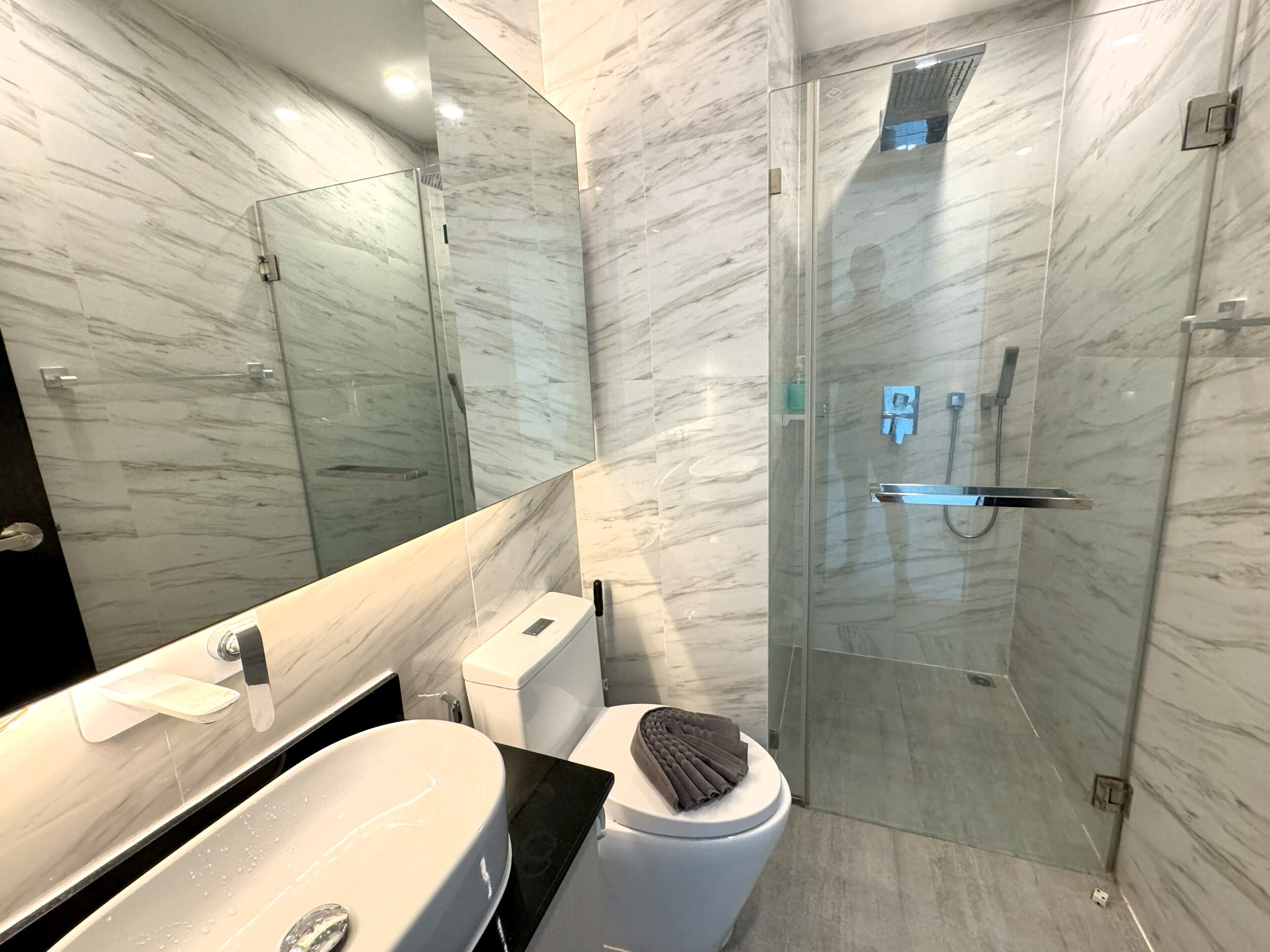 Ein modernes Badezimmer mit Marmorwand, einer gläsernen Dusche, einer weißen Toilette und einem Waschbecken mit schwarzer Arbeitsplatte.