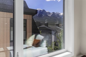 A room with a view of mountains through a window, a white sofa, and a wooden wall.