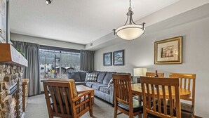 A cozy living room with a stone fireplace, a gray sofa, wooden chairs, and a dining table.