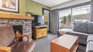 A cozy living room with a stone fireplace, a television, and a large window with curtains.