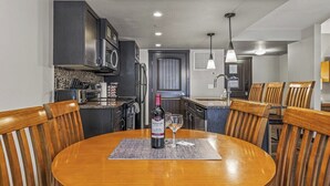 A modern kitchen with dark cabinets, a central island, and a dining area with wooden chairs and a round table.