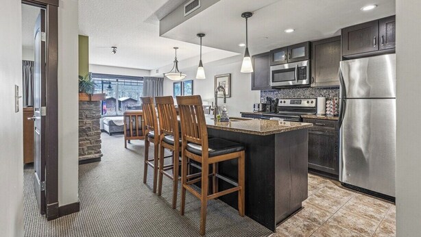A modern kitchen with a central island, dark cabinetry, stainless steel appliances, and pendant lighting.